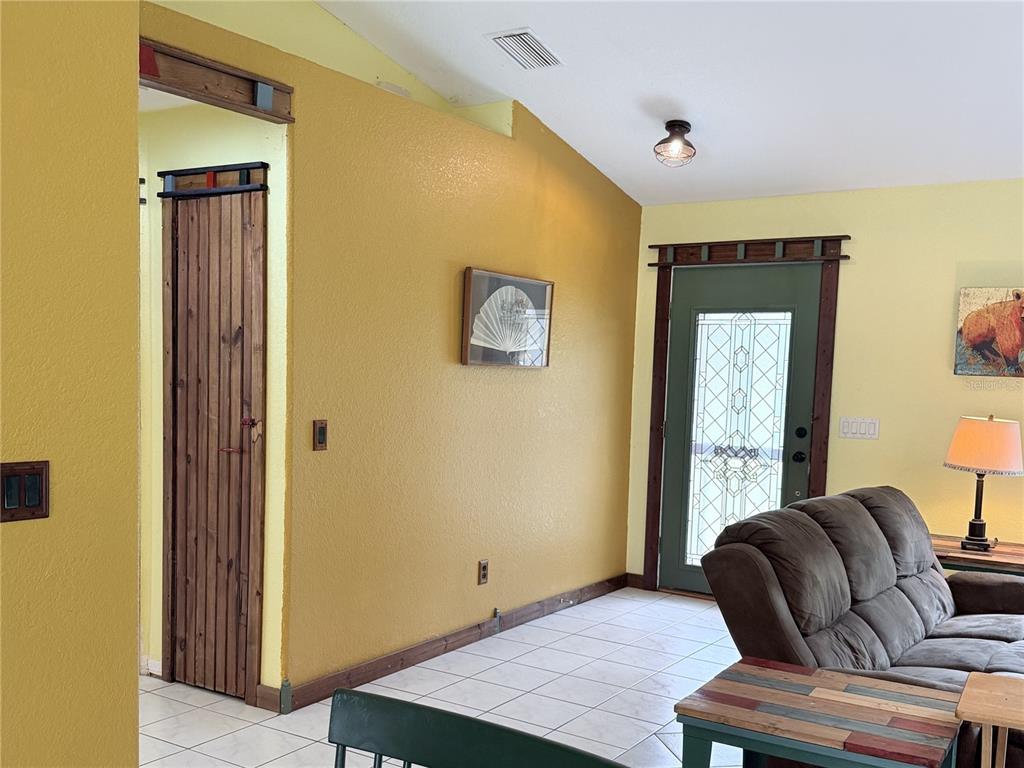 A living room features yellow walls, a vaulted ceiling, a wooden door, and tiled flooring — 6345 BODMIN LANE, NORTH PORT, FL