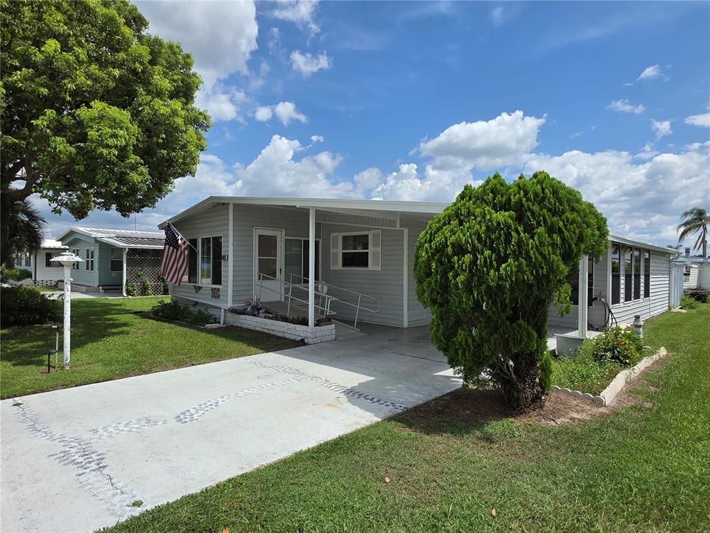 A light gray manufactured home features a concrete driveway, a carport, and a wheelchair ramp — 5634 ARROWHEAD DRIVE, ZEPHYRHILLS, FL