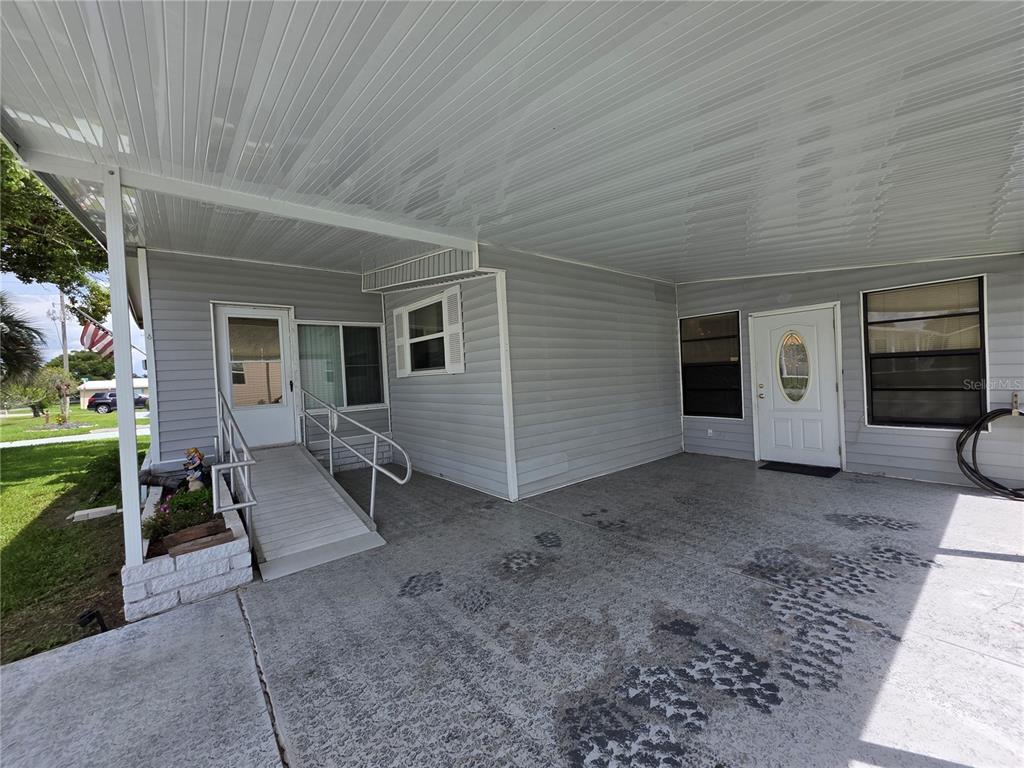 A covered carport features a concrete floor, a wheelchair ramp, and two exterior doors — 5634 ARROWHEAD DRIVE, ZEPHYRHILLS, FL
