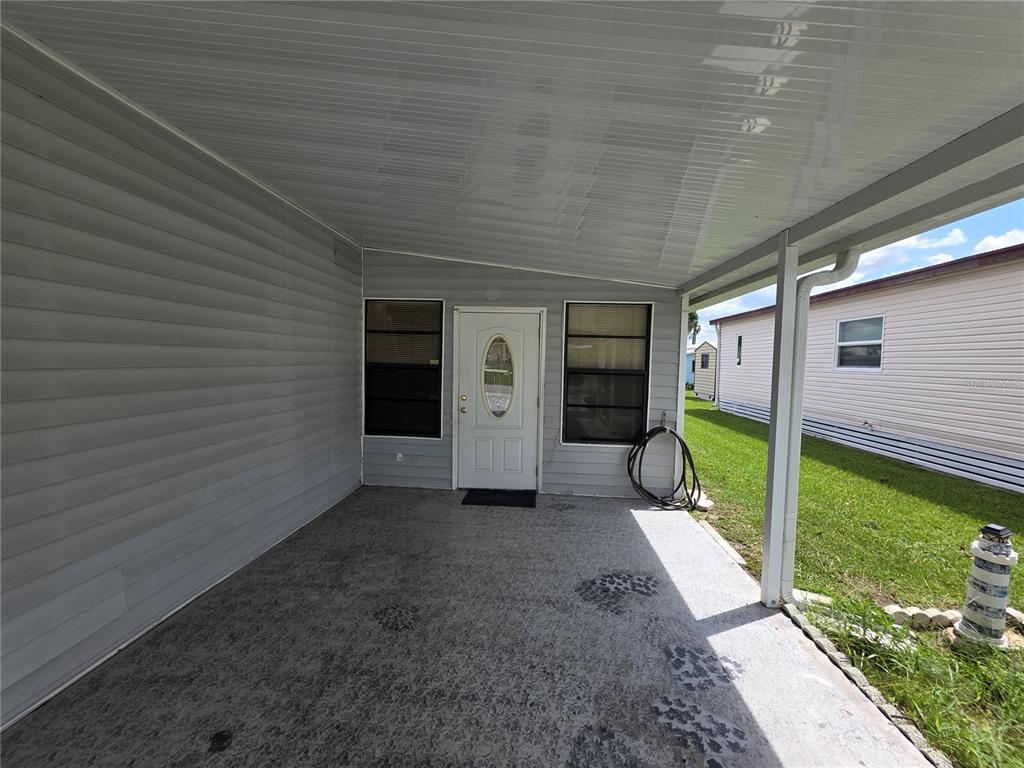 A covered concrete patio features gray siding, a white front door, and a support post — 5634 ARROWHEAD DRIVE, ZEPHYRHILLS, FL