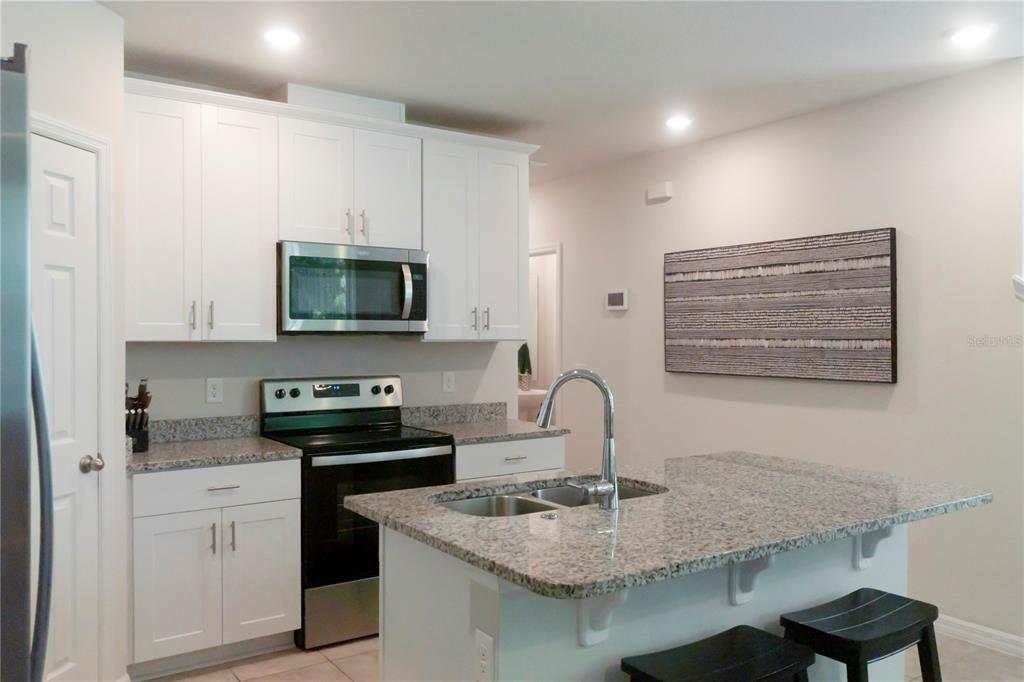 A kitchen with white cabinets, granite countertops, a stainless steel microwave, and a center island — 1610 GRAND RUE DRIVE, CASSELBERRY, FL