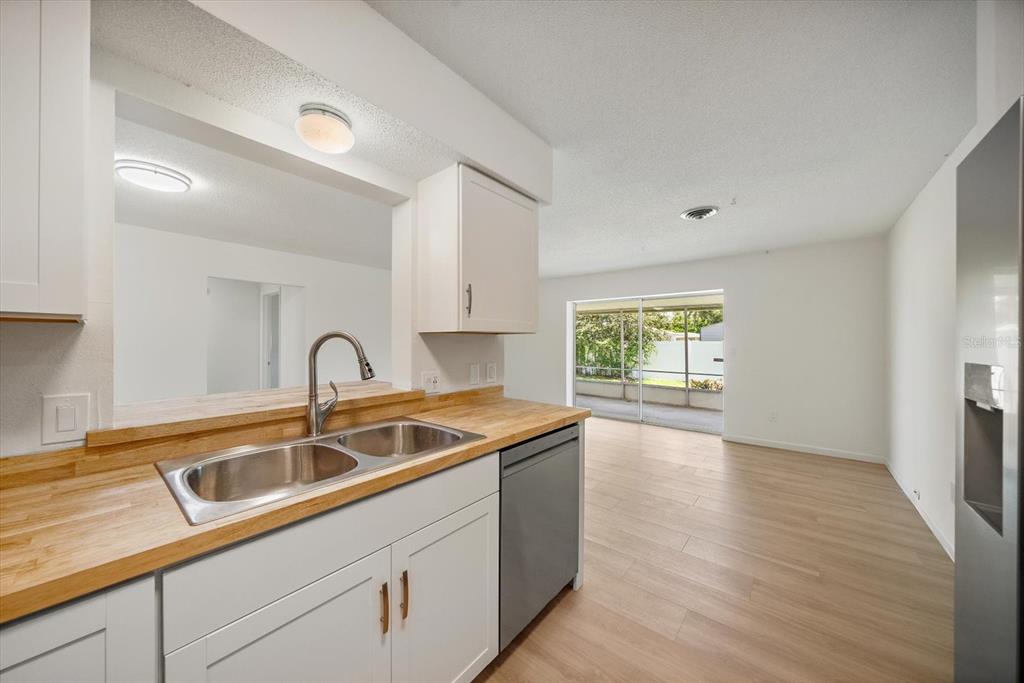 A kitchen with wood countertops and a stainless steel sink overlooks a bright living area — 987 QUEEN ROAD, VENICE, FL