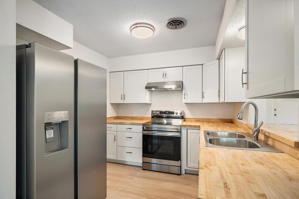 A kitchen features stainless steel appliances, white cabinetry, and light wood butcher block countertops — 987 QUEEN ROAD, VENICE, FL