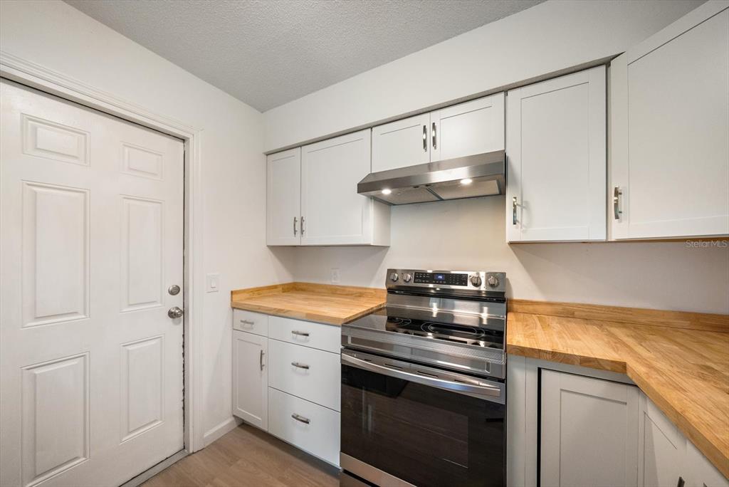 A kitchen features white cabinets, butcher block countertops, and a stainless steel stove — 987 QUEEN ROAD, VENICE, FL