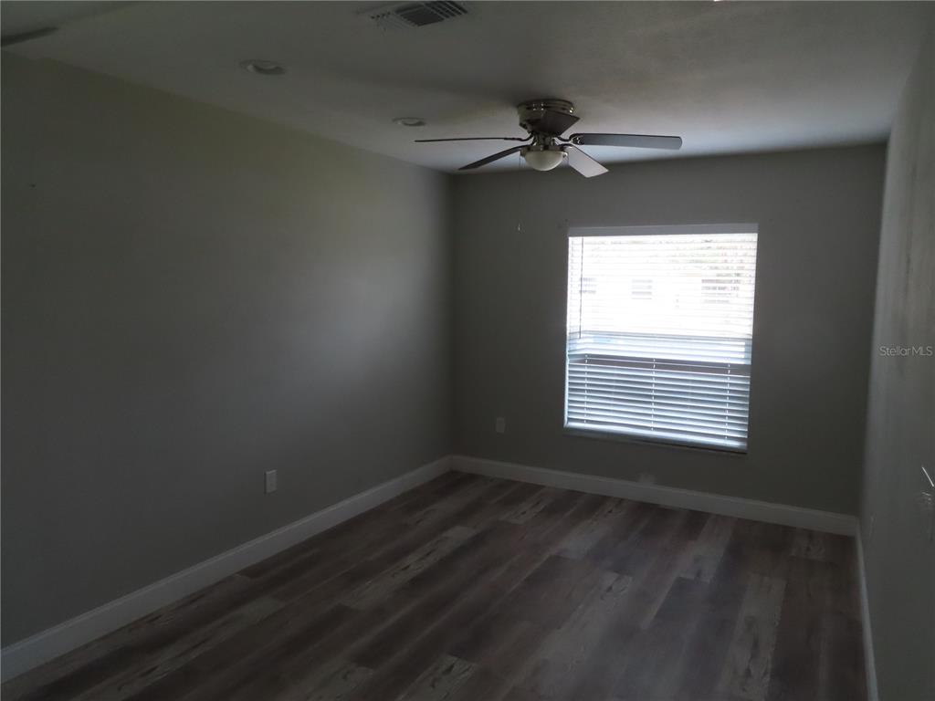 An empty bedroom features gray walls, wood-look flooring, a ceiling fan, and a window — 1215 WINDSOR CIRCLE, BRANDON, FL