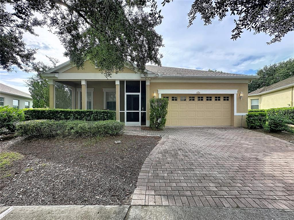 A single-story house features a tan stucco exterior, a screened front porch, and a brick driveway — 122 FLAME VINE WAY, GROVELAND, FL