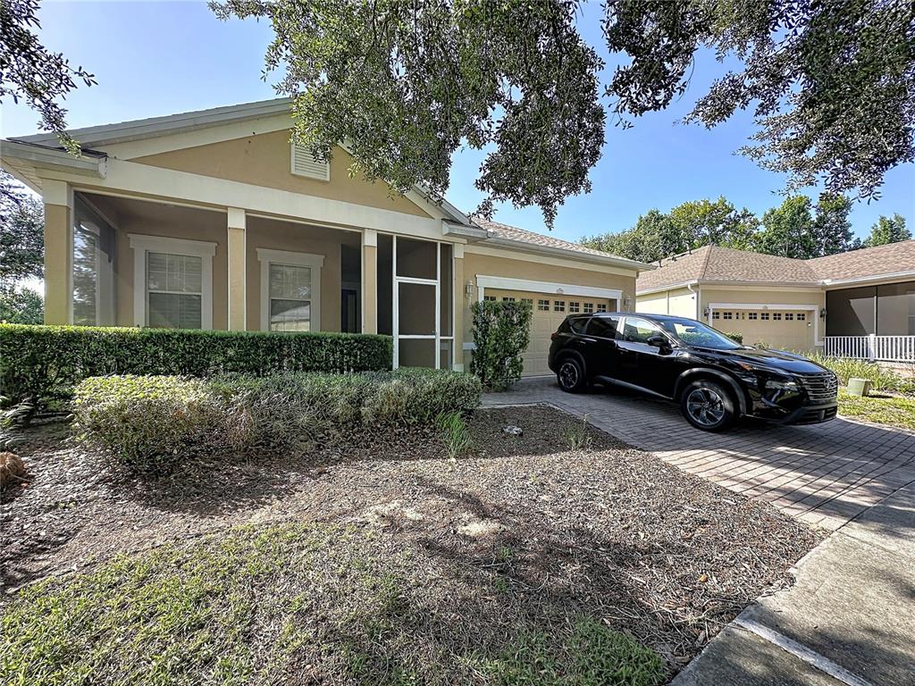 A single-story house features a tan stucco exterior, a screened front porch, and a brick driveway — 122 FLAME VINE WAY, GROVELAND, FL