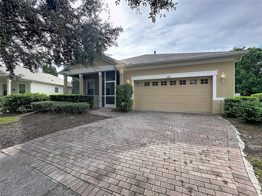 A single-story house with a tan stucco exterior, a brick paver driveway, and a garage — 122 FLAME VINE WAY, GROVELAND, FL