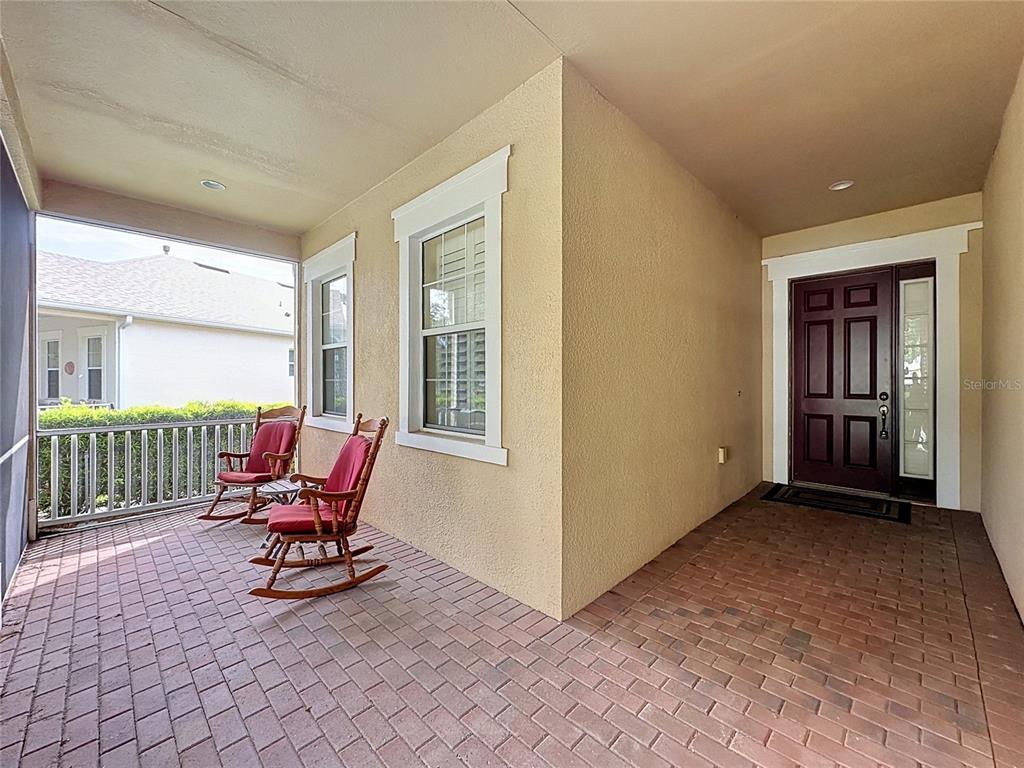 A covered porch features brick flooring, two wooden rocking chairs, and a dark front door — 122 FLAME VINE WAY, GROVELAND, FL