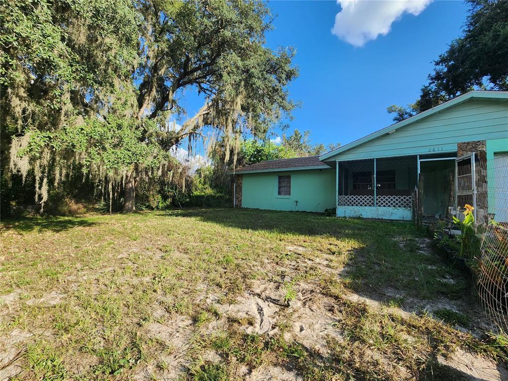 A light green house with a screened-in porch sits next to a large, moss-covered tree — 2871 W ALBATROSS ROAD, AVON PARK, FL