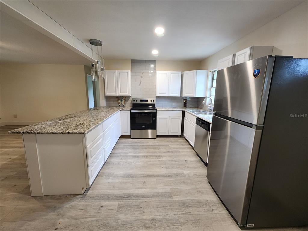 A kitchen features white cabinets, granite countertops, stainless steel appliances, and light wood-look flooring — 2871 W ALBATROSS ROAD, AVON PARK, FL