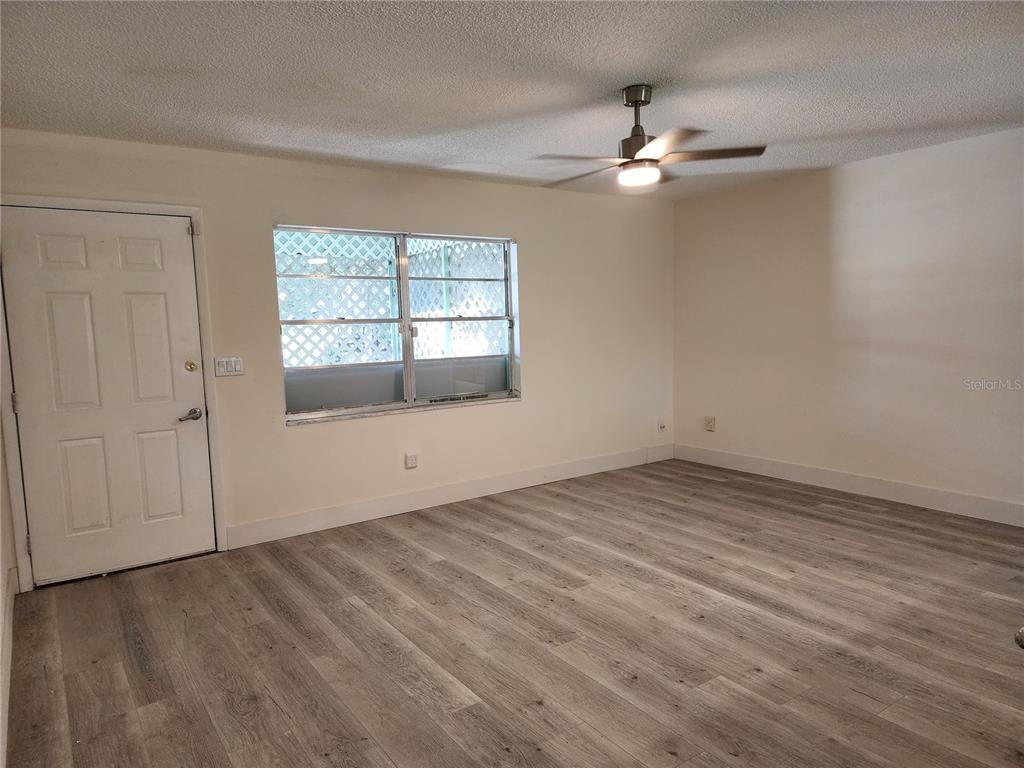 An empty room features light wood-look flooring, a ceiling fan, and a white entry door — 2871 W ALBATROSS ROAD, AVON PARK, FL