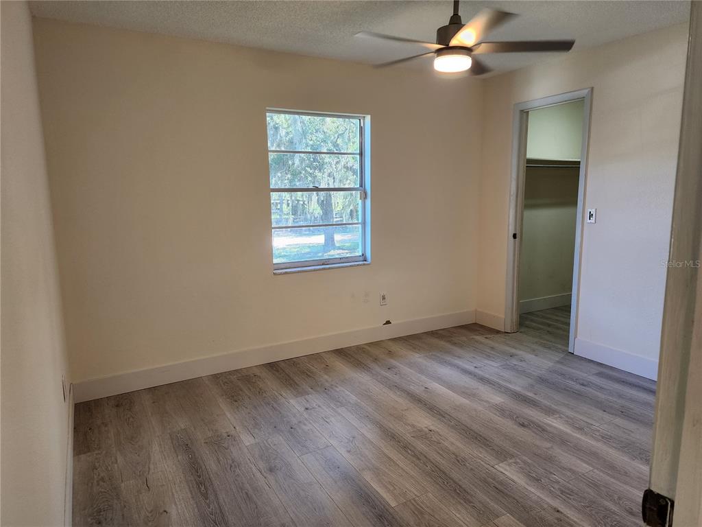 An empty bedroom features light-colored walls, wood-look flooring, a ceiling fan, and a walk-in closet — 2871 W ALBATROSS ROAD, AVON PARK, FL