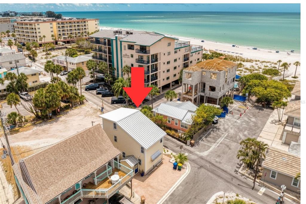 An aerial view shows a yellow multi-story house with a metal roof near the beach — 13095 GULF LANE, MADEIRA BEACH, FL