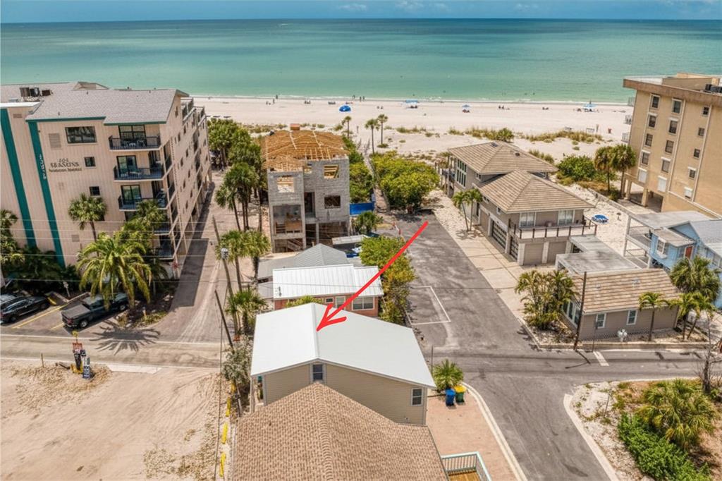An aerial view shows a tan house with a metal roof near a sandy beach — 13095 GULF LANE, MADEIRA BEACH, FL