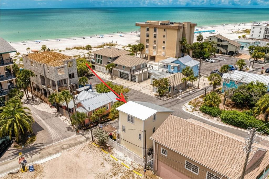 An aerial view shows a yellow multi-story house near a beach with other nearby buildings — 13095 GULF LANE, MADEIRA BEACH, FL