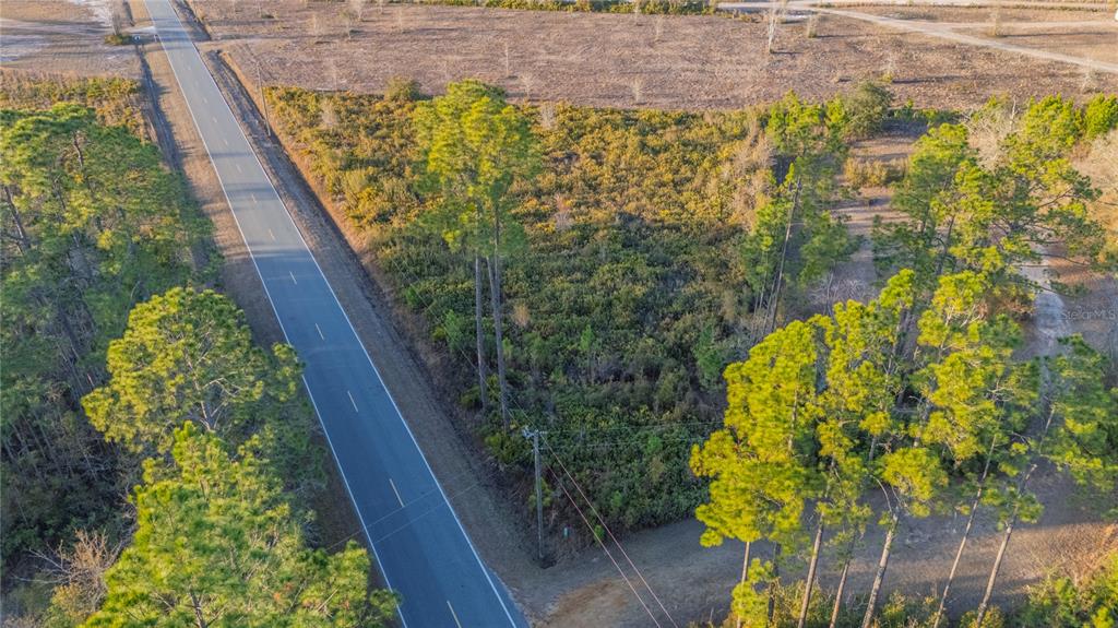 An aerial view shows a paved road running alongside a wooded, undeveloped plot of land — 0 CONNER NELSON ROAD, HILLIARD, FL