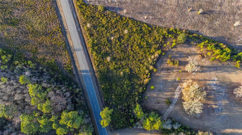 An aerial view shows a paved road running alongside a wooded lot and open field — 0 CONNER NELSON ROAD, HILLIARD, FL