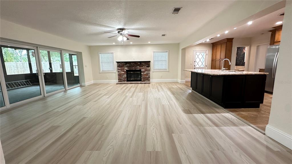 An open-concept living room features light wood-look flooring, a brick fireplace, and a kitchen island — 1850 JUAREZ WAY S, ST PETERSBURG, FL