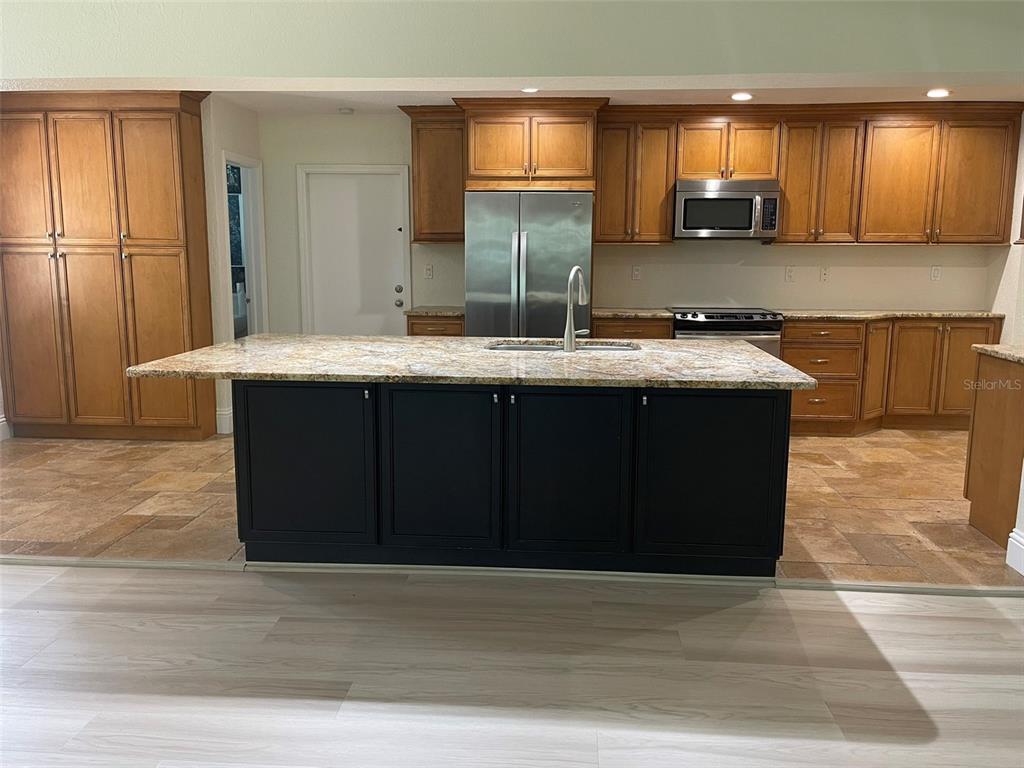 A kitchen features wood cabinets, a granite-topped island with black base, and tile flooring — 1850 JUAREZ WAY S, ST PETERSBURG, FL
