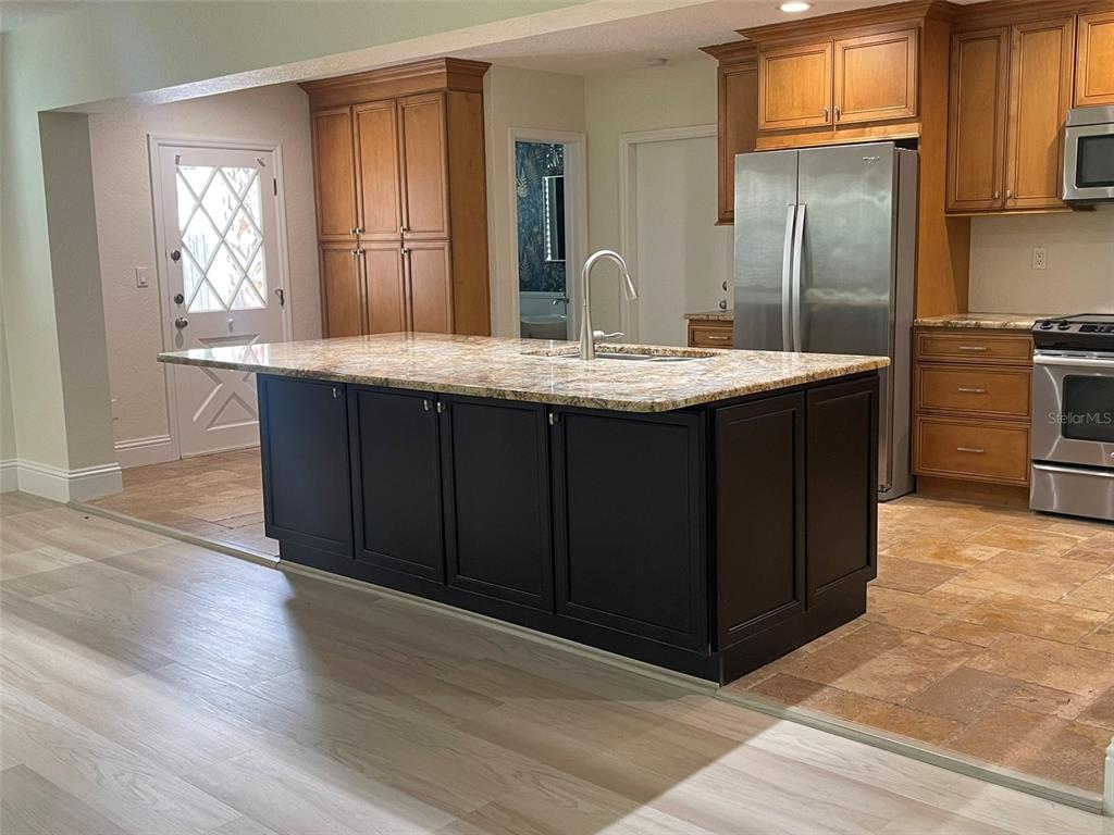 A kitchen features a dark island with a granite countertop, wood cabinets, and tile flooring — 1850 JUAREZ WAY S, ST PETERSBURG, FL