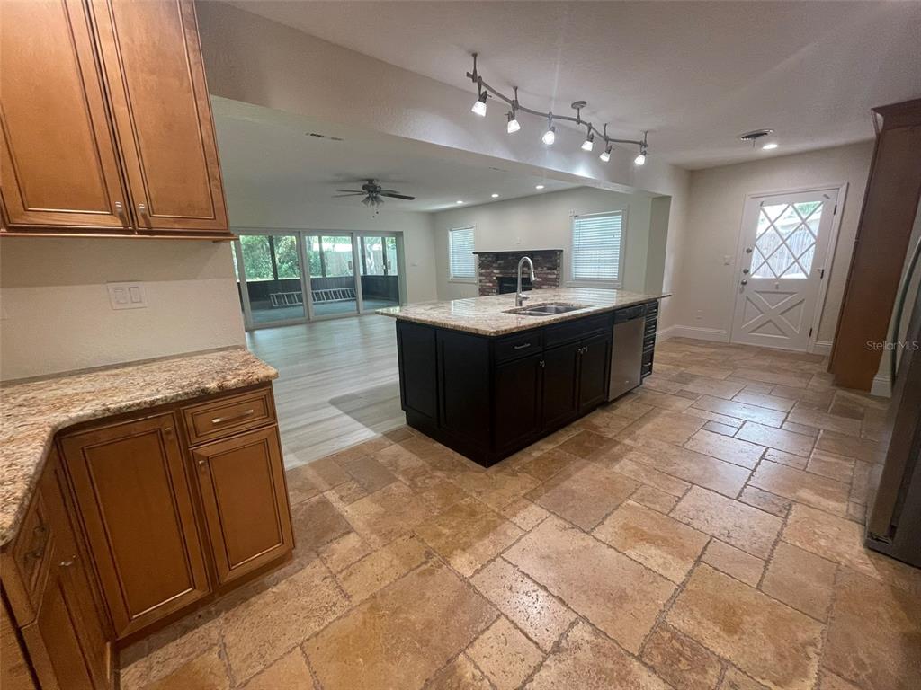 A kitchen with wood cabinets, a dark island, and tile flooring opens to a living area — 1850 JUAREZ WAY S, ST PETERSBURG, FL