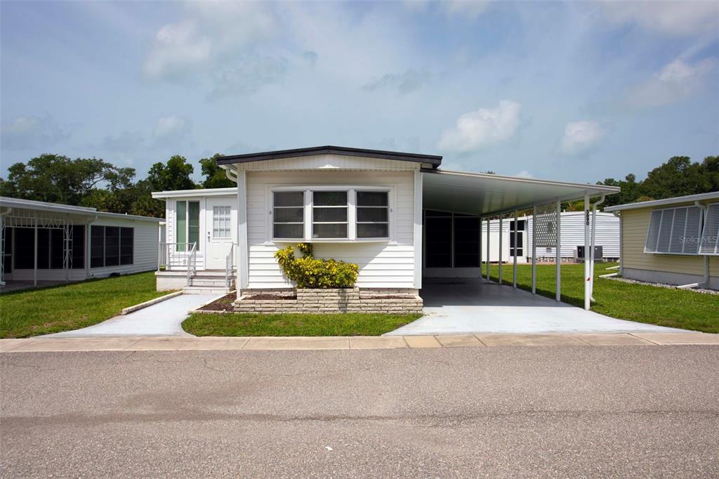 A white mobile home with a carport and a small front garden under a blue sky — 5690 FORSYTHIA ROAD, VENICE, FL