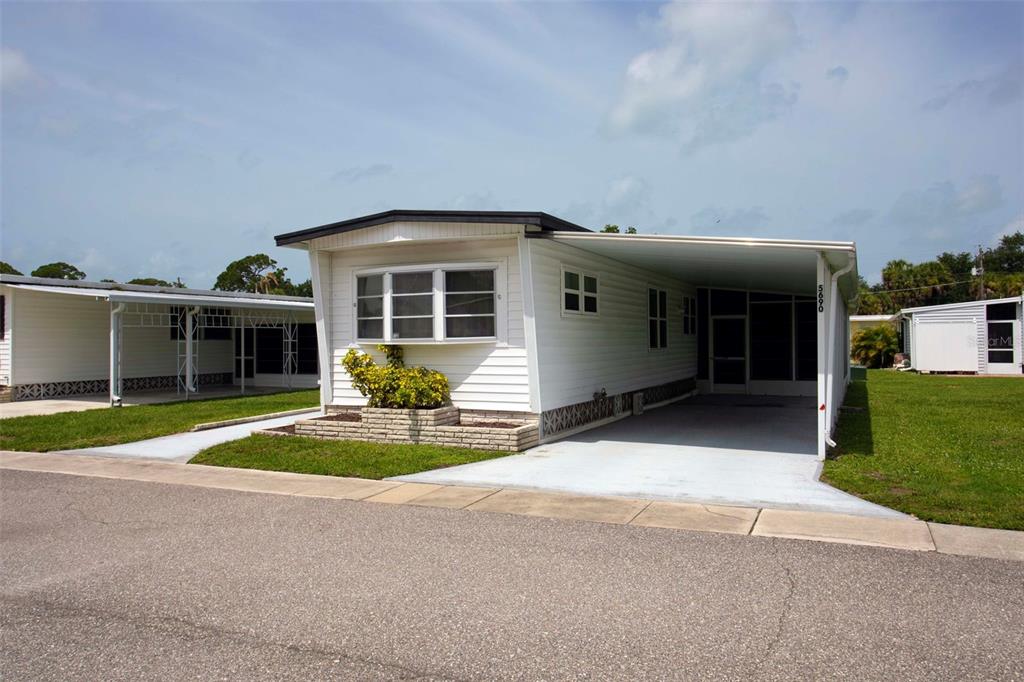 A white mobile home features a carport, a front bay window, and a brick planter — 5690 FORSYTHIA ROAD, VENICE, FL