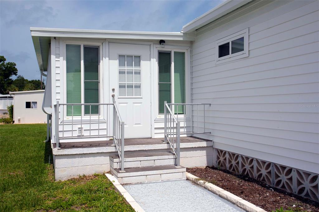 A white mobile home exterior features a small porch with metal railings and steps — 5690 FORSYTHIA ROAD, VENICE, FL