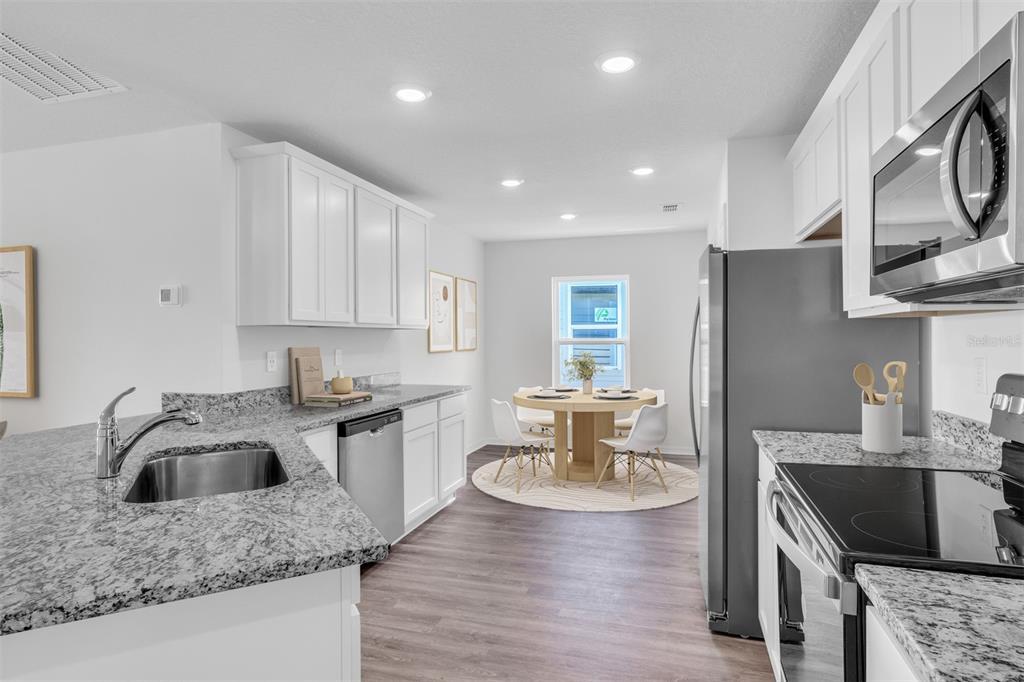 A kitchen with white cabinets, granite countertops, stainless steel appliances, and a dining area — 40 PRESIDENTIAL LANE, PALM COAST, FL