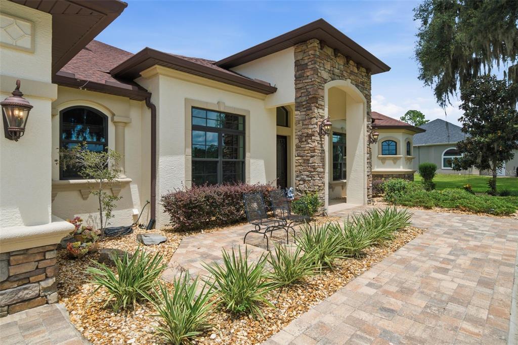 A stone-accented house exterior features a paved walkway, landscaping, and a covered entryway with chairs — 10994 N RIVER RANCH PATH, CRYSTAL RIVER, FL