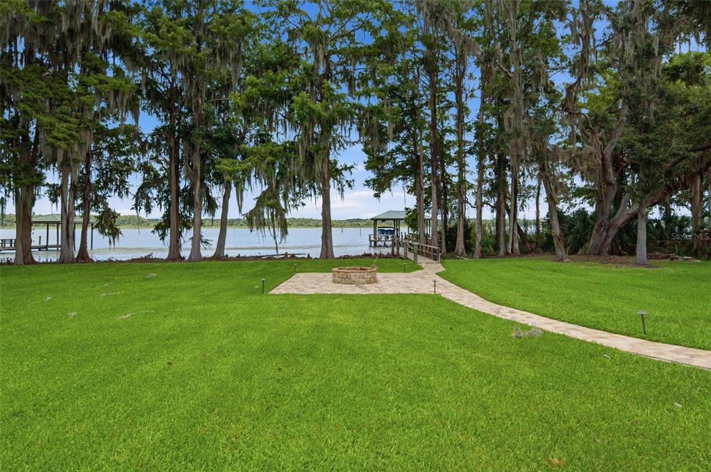 A grassy backyard features a stone fire pit area and a walkway leading to a dock — 10994 N RIVER RANCH PATH, CRYSTAL RIVER, FL