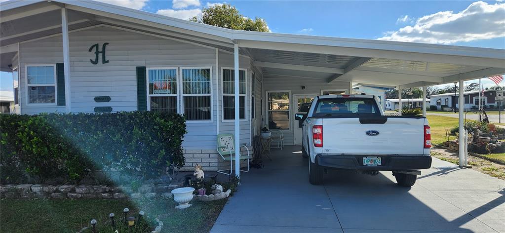 A light-colored manufactured home features a large attached carport with a white pickup truck parked — 36330 LE SABRE WAY, ZEPHYRHILLS, FL