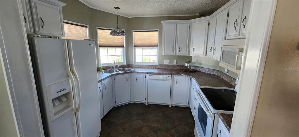 A kitchen with white cabinets, brown countertops, a white refrigerator, and a corner sink — 36330 LE SABRE WAY, ZEPHYRHILLS, FL