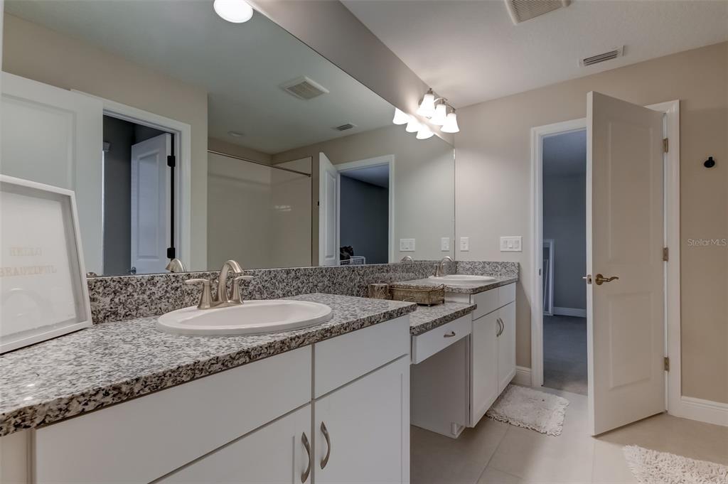 A bathroom features a double vanity with granite countertops, white cabinets, and a large mirror — 13118 JETER CREEK DRIVE, RIVERVIEW, FL