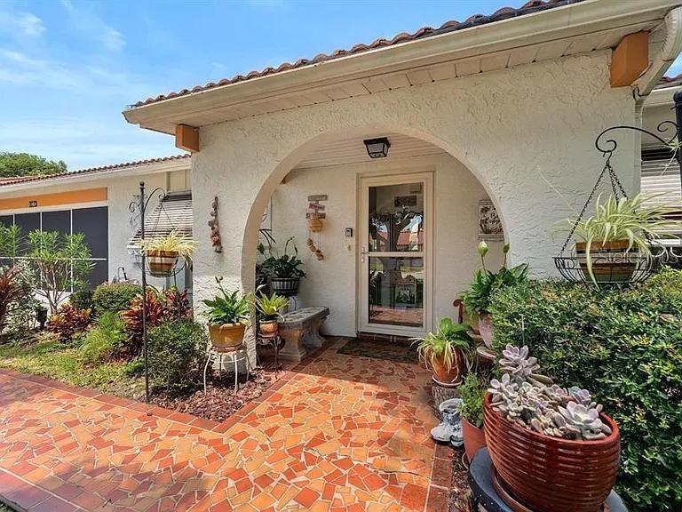 A stucco house exterior features a tiled entryway, an arched porch, and numerous potted plants — 11404 STANSBERRY DRIVE, PORT RICHEY, FL