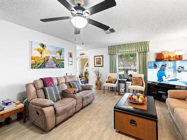 A living room features a brown reclining sofa, a coffee table, and a ceiling fan — 11404 STANSBERRY DRIVE, PORT RICHEY, FL