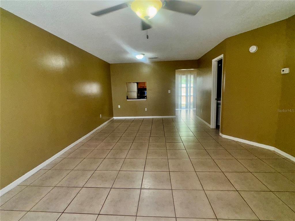 An empty room with tan walls, tile flooring, a ceiling fan, and a kitchen pass-through — 1605 SHADY RIDGE COURT, ORLANDO, FL