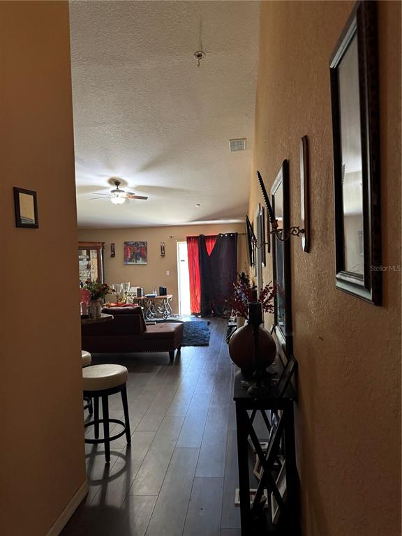 A hallway with dark wood-look flooring leads into a living room with a ceiling fan — 116 SPOONBILL COURT, KISSIMMEE, FL