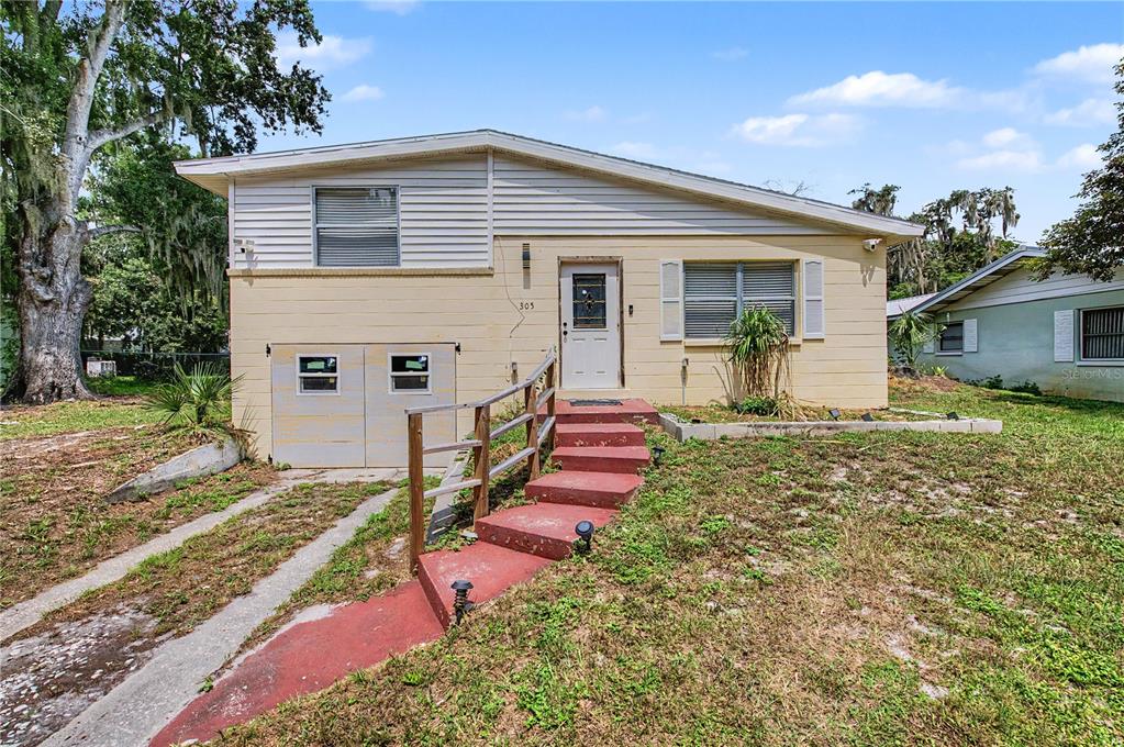 A one-story house with yellow siding, a front staircase, and a lower-level garage door — 305 CORDOVA ROAD, AUBURNDALE, FL