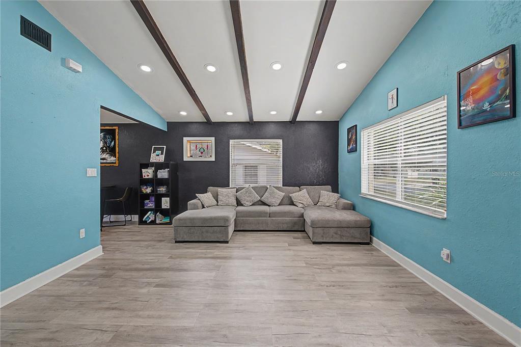 A living room features light blue walls, a dark accent wall, wood ceiling beams, and gray flooring — 305 CORDOVA ROAD, AUBURNDALE, FL