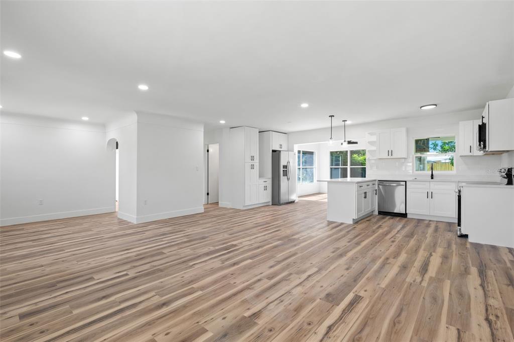 An open-concept kitchen and living area features white cabinetry, stainless steel appliances, and wood-look flooring — 6116 52ND AVENUE N, KENNETH CITY, FL