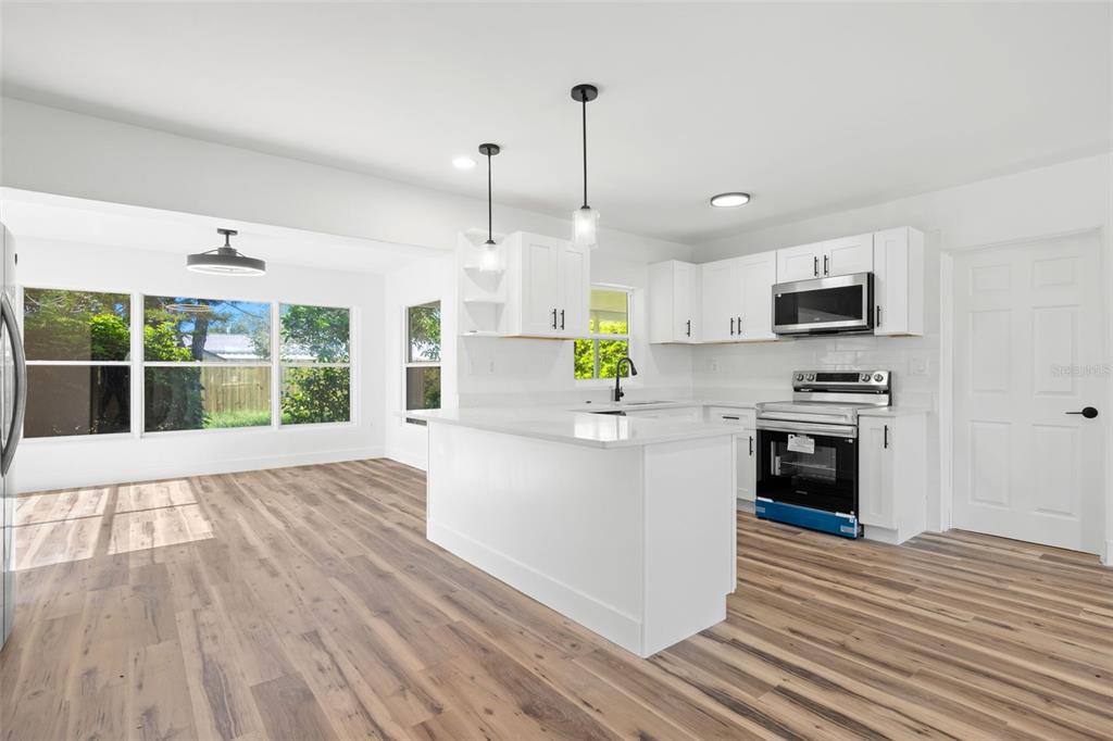 A bright kitchen features white cabinets, a central island, and wood-look flooring — 6116 52ND AVENUE N, KENNETH CITY, FL