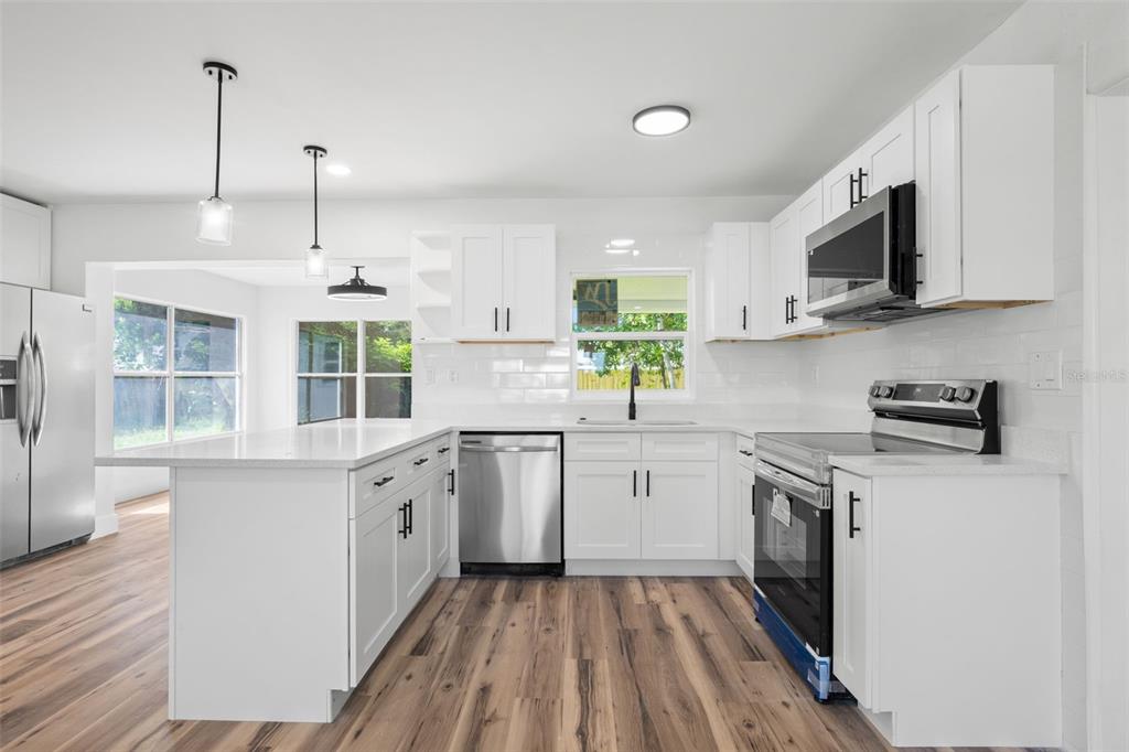 A modern kitchen features white cabinets, stainless steel appliances, a peninsula, and wood-look flooring — 6116 52ND AVENUE N, KENNETH CITY, FL