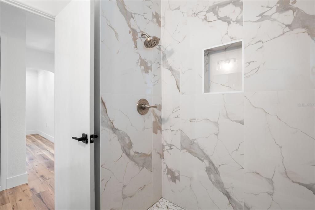 A walk-in shower features white marble-look wall tiles, a built-in niche, and a showerhead — 6116 52ND AVENUE N, KENNETH CITY, FL