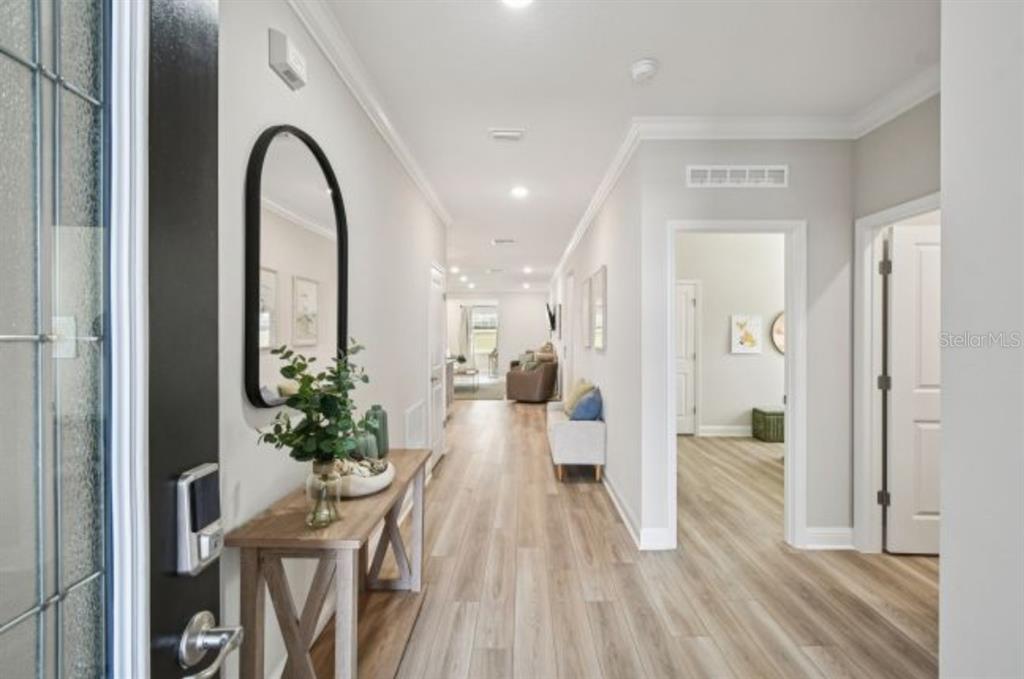 A bright entryway features light wood-look flooring, a console table, and a tall arched mirror — 6089 CHORUS DRIVE, MASCOTTE, FL