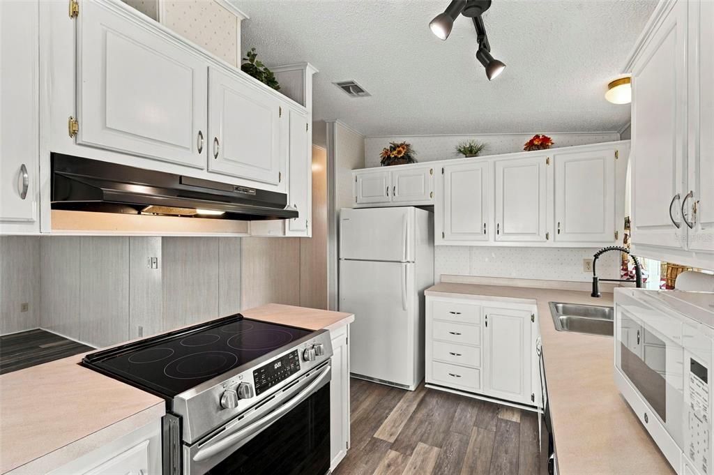 A kitchen features white cabinets, a stainless steel electric stove, and light-colored laminate countertops — 340 CANAL WAY, OLDSMAR, FL