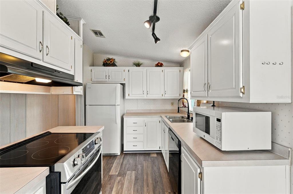 A kitchen features white cabinets, a white refrigerator, a black stove, and wood-look flooring — 340 CANAL WAY, OLDSMAR, FL