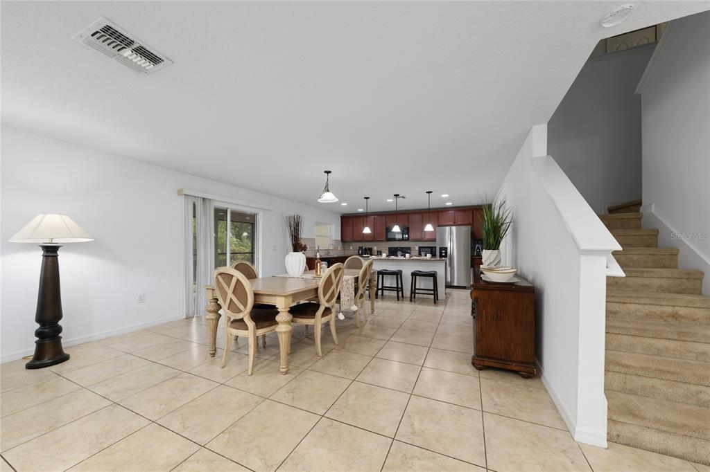 An open-concept dining area and kitchen feature tile flooring, wooden cabinetry, and a carpeted staircase — 4752 BLUE DIAMOND STREET, KISSIMMEE, FL