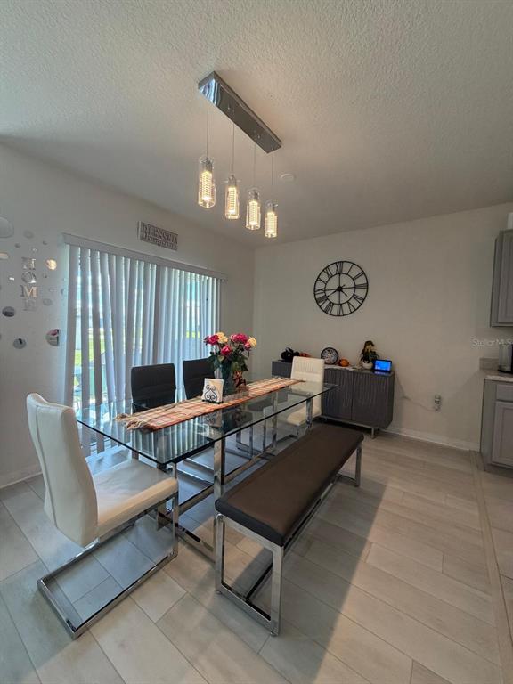 A dining area features a glass-topped table, white chairs, a bench, and a modern light fixture — 332 AUBURN GROVE CROSSING, AUBURNDALE, FL